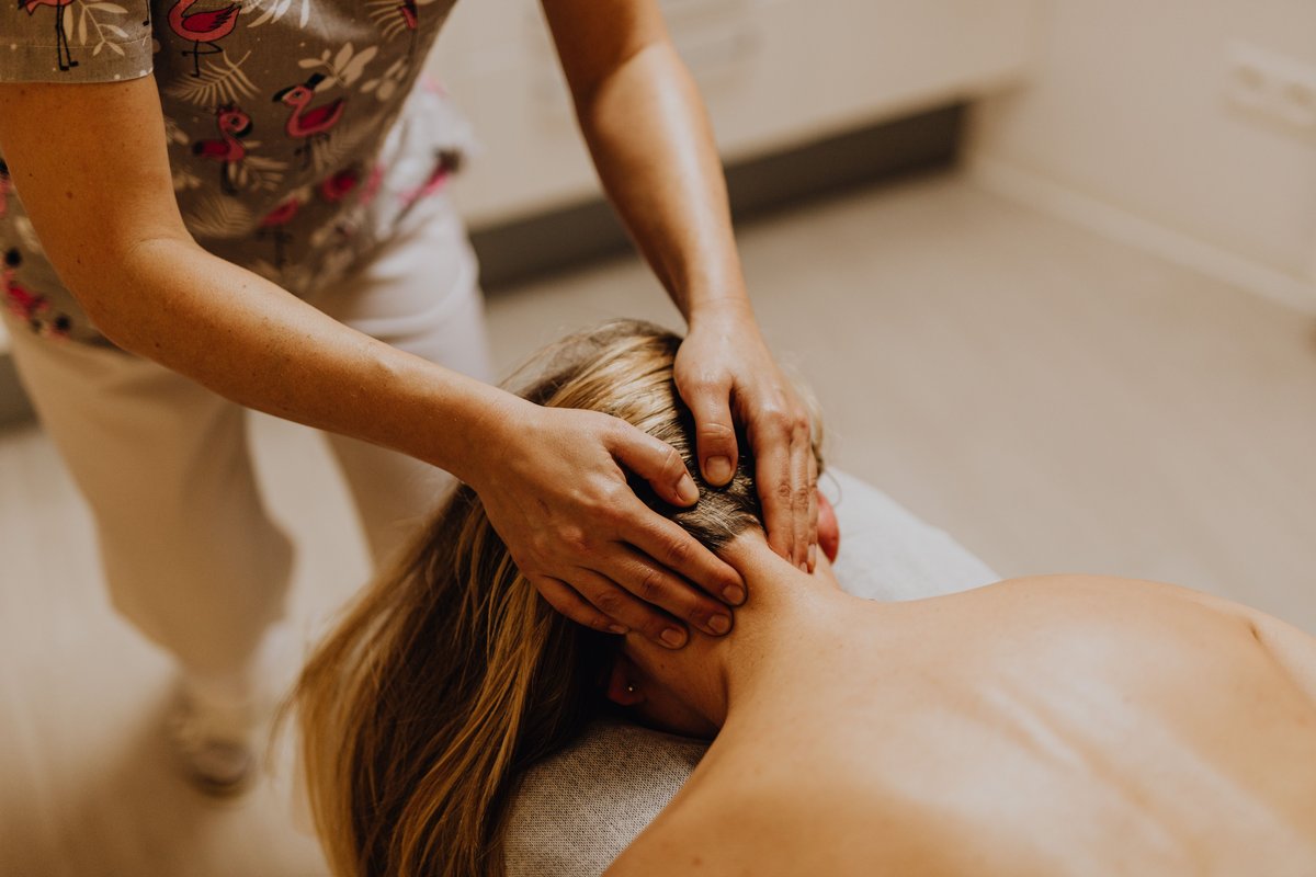 Therapist in flamingo-print scrubs pressing both hands into the back of a woman's neck as she lies face down on a massage table